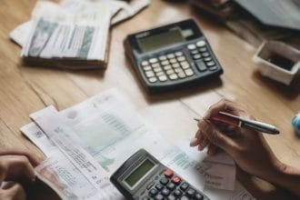 Bàn tay tính toán lãi suất vay bằng máy tính cầm tay, hợp đồng vay và tiền trên bàn