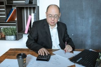 Vay tín chấp VPBank Techcombank so sánh 2026: Asian businessman working with calculator and notes at his desk in a modern office space.