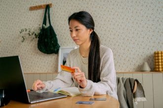 Nữ nhân viên châu Á dùng laptop và thẻ tín dụng mua sắm online tại nhà — minh họa mở thẻ tín dụng cho người lương 7 triệu