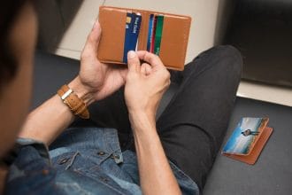 So sánh thẻ tín dụng và thẻ ghi nợ: A close-up of a man holding a wallet containing credit cards and an ID inside a room.