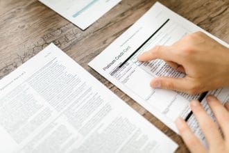 Phí thường niên thẻ tín dụng: A hand examining a credit card agreement on a wooden desk, highlighting financial review.